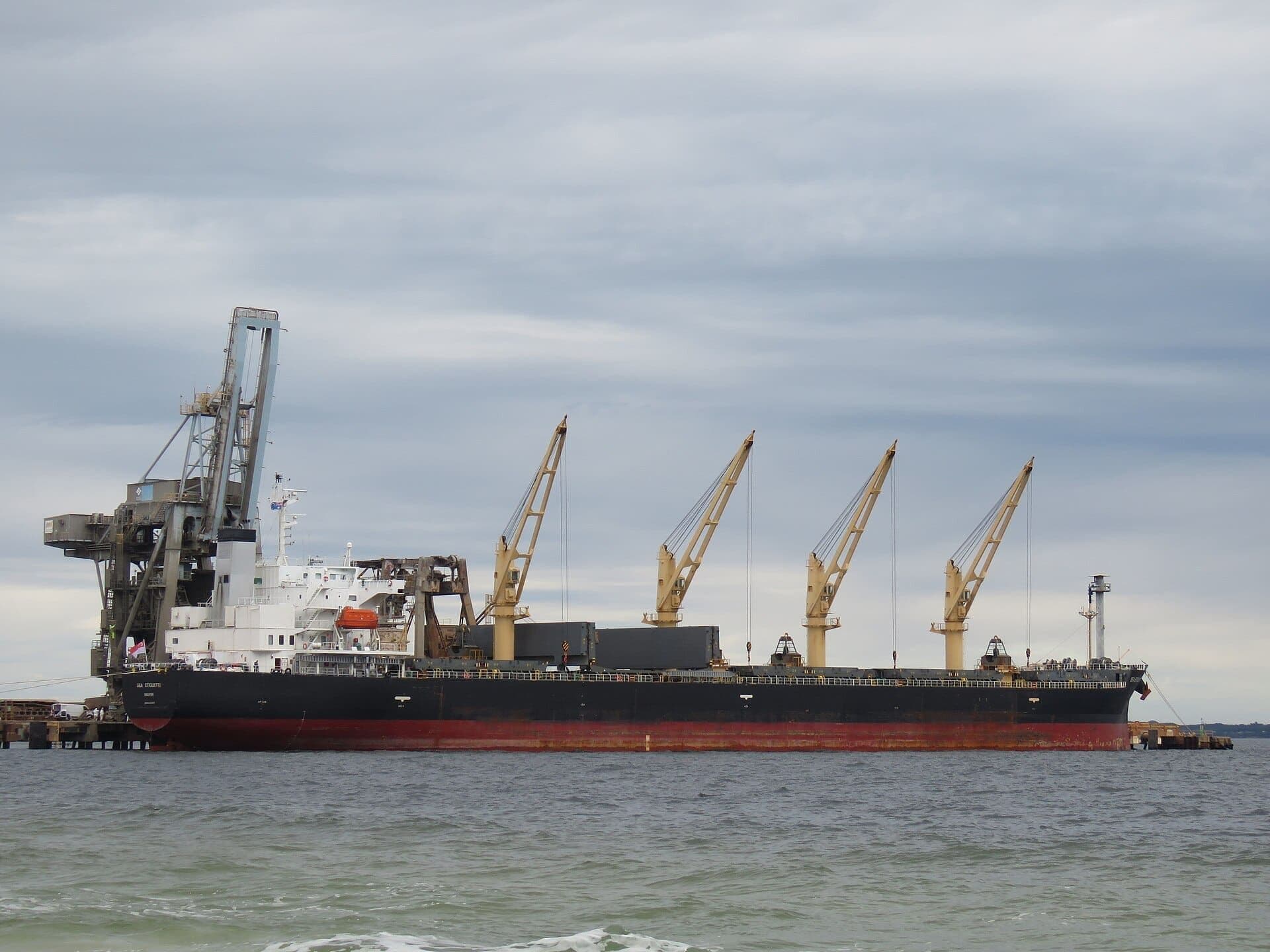 A bulk carrier alongside a terminal with cargo cranes raised during port operations