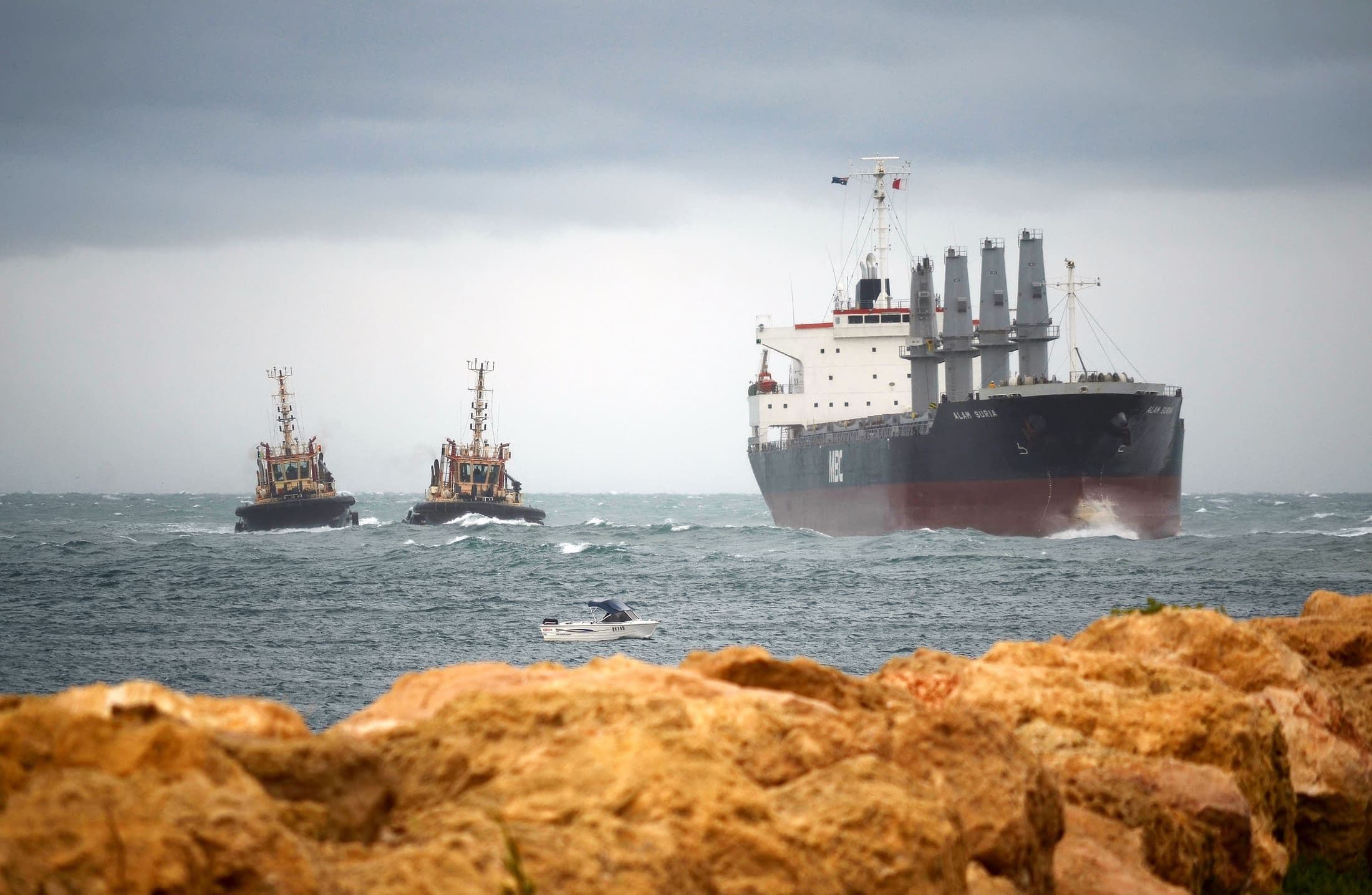 A bulk carrier underway at sea escorted by tugboats in open water